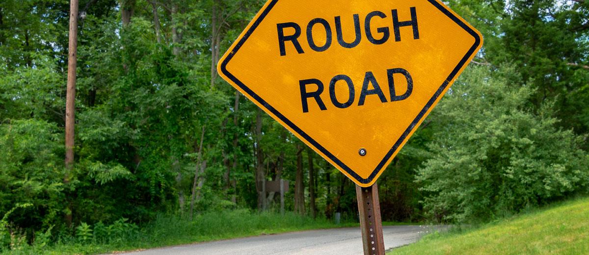 A close-up shot of a yellow road sign that says "rough road."