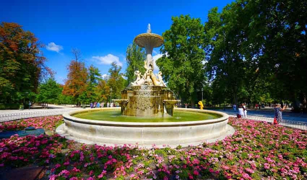 A fountain in a park surrounded by flowers.