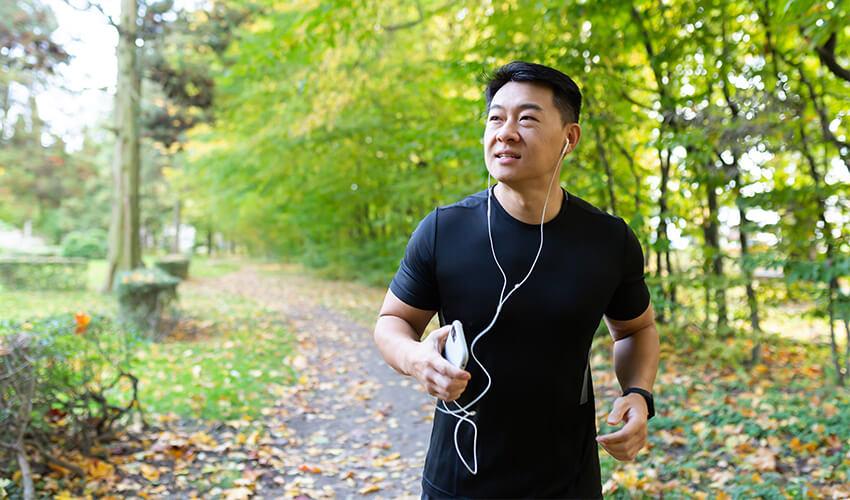 A man jogging in a park with earphones.