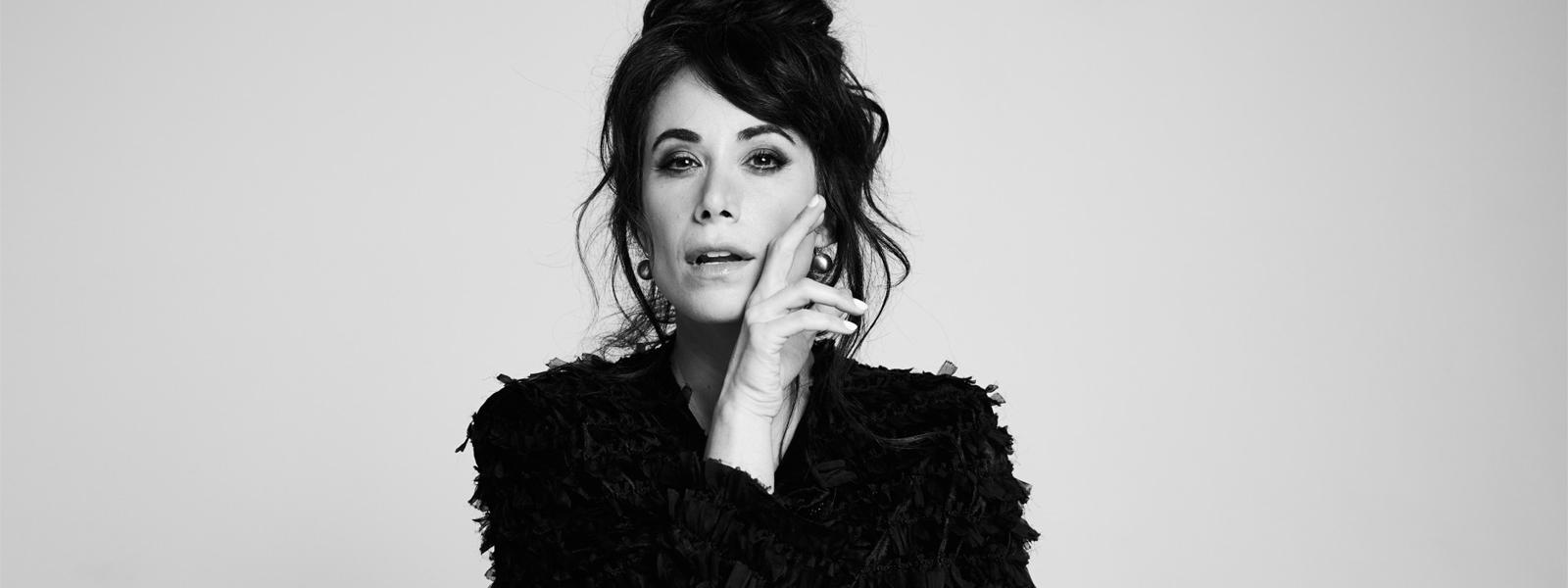 A black and white image of a woman wearing a black blouse looking directly at the camera.