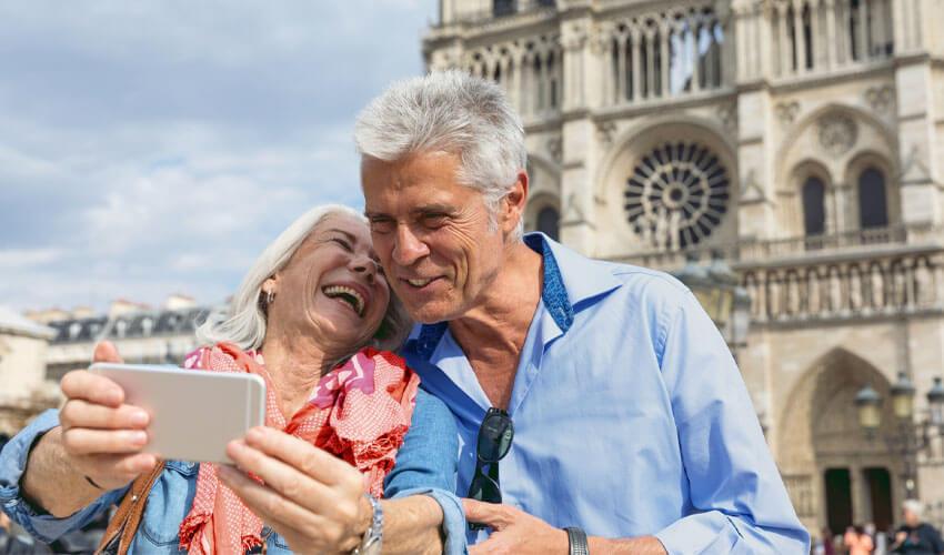 An older couple taking a selfie in front of the notre dame cathedral.