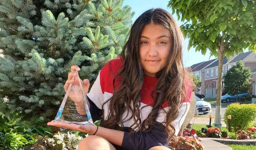 A young girl holding an award in front of a tree.