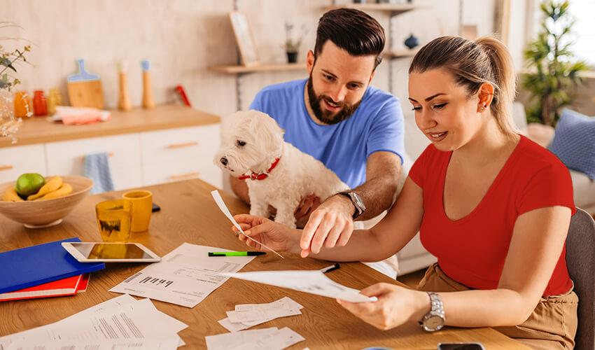 A man and woman sitting at a table with papers and a dog.