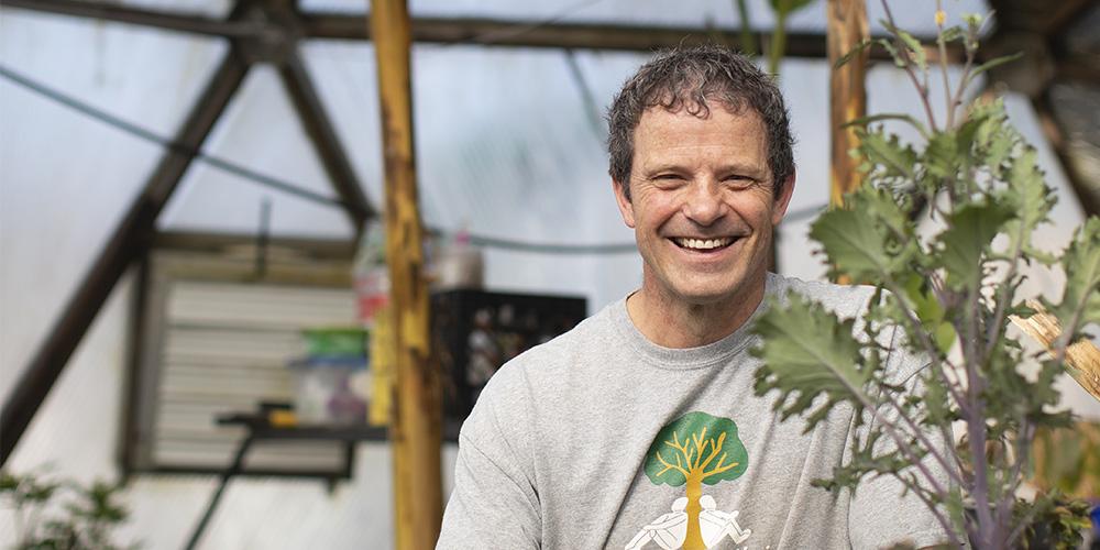 A smiling person standing in a greenhouse surrounded by plants.