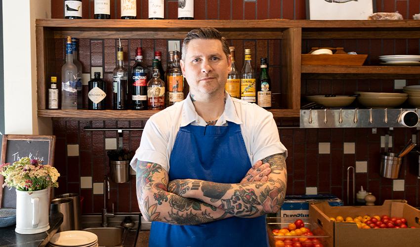 A man in a blue apron standing in front of a counter.