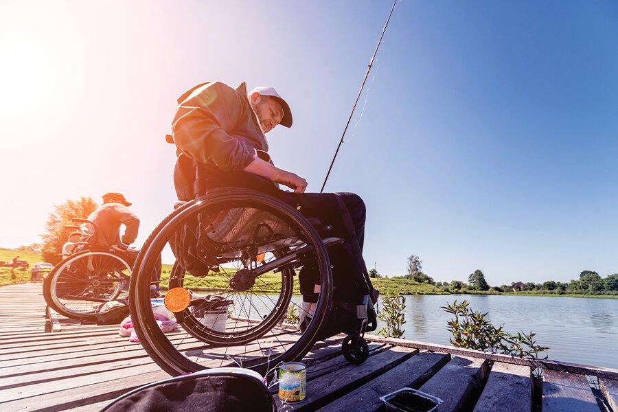 A person in a wheelchair fishing off a dock on a sunny day.