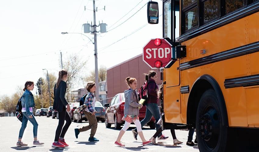 A group of people crossing a street near a school bus.