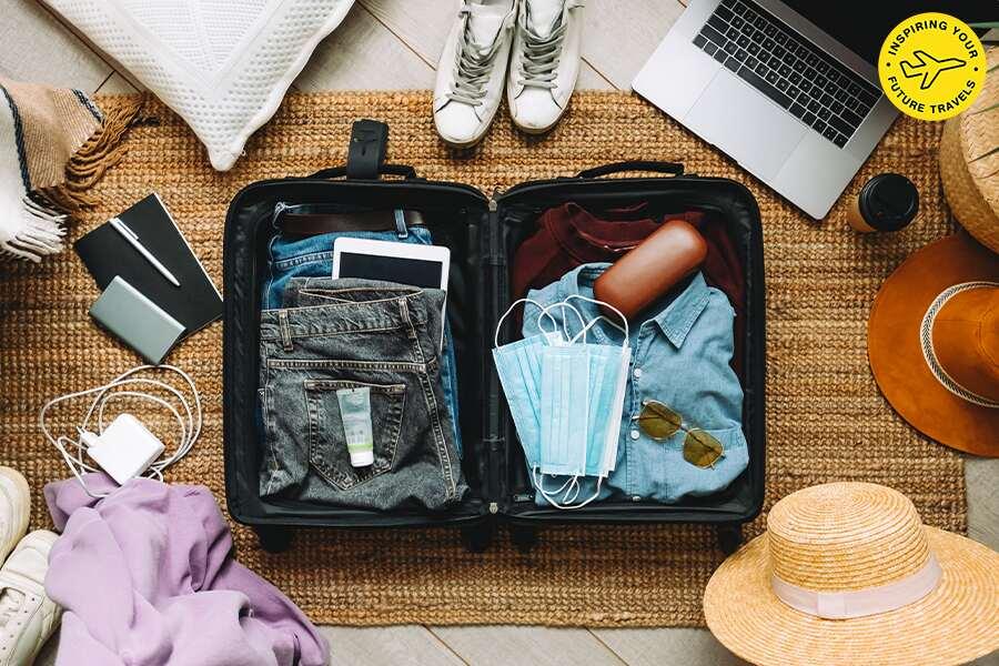 A suitcase with a laptop, hat, sunglasses and other items on a rug.