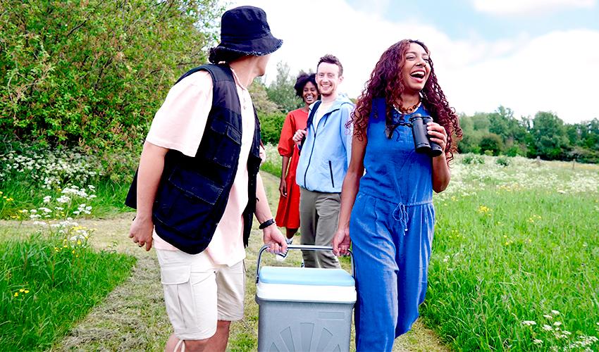 A group of four adults walking on a trail, one is holding a cooler.