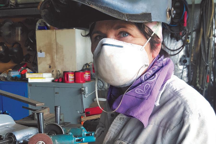 A person wearing protective welding gear and a dust mask in a workshop environment.