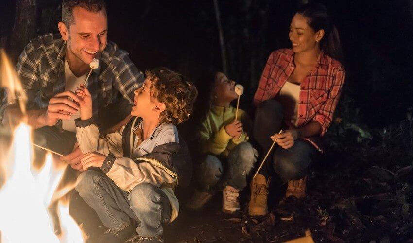 A family is sitting around a campfire at night.