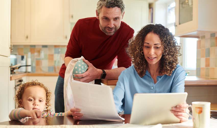 A man, woman and child are looking at a tablet in the kitchen.