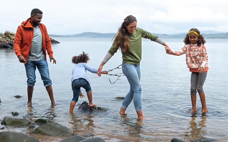 Family of four playing in a lake with their pants rolled up.