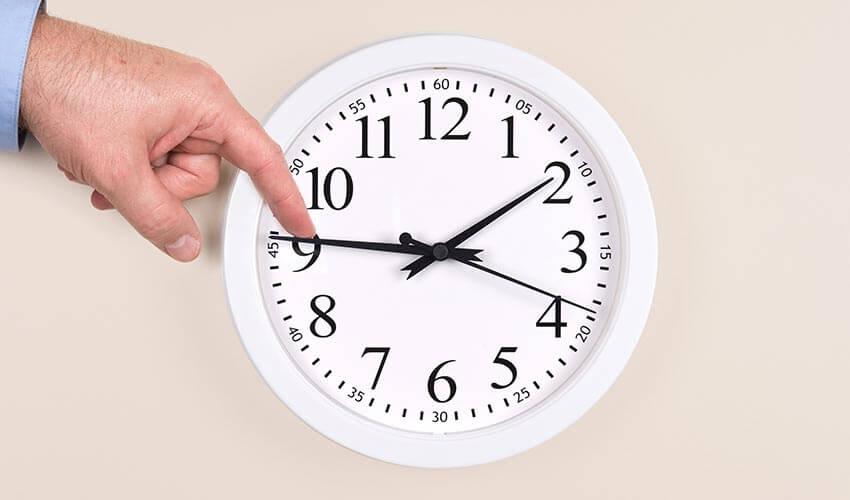 A man's hand pointing at a clock on a wall.