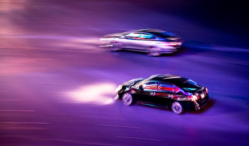 Two cars driving on a street at night.