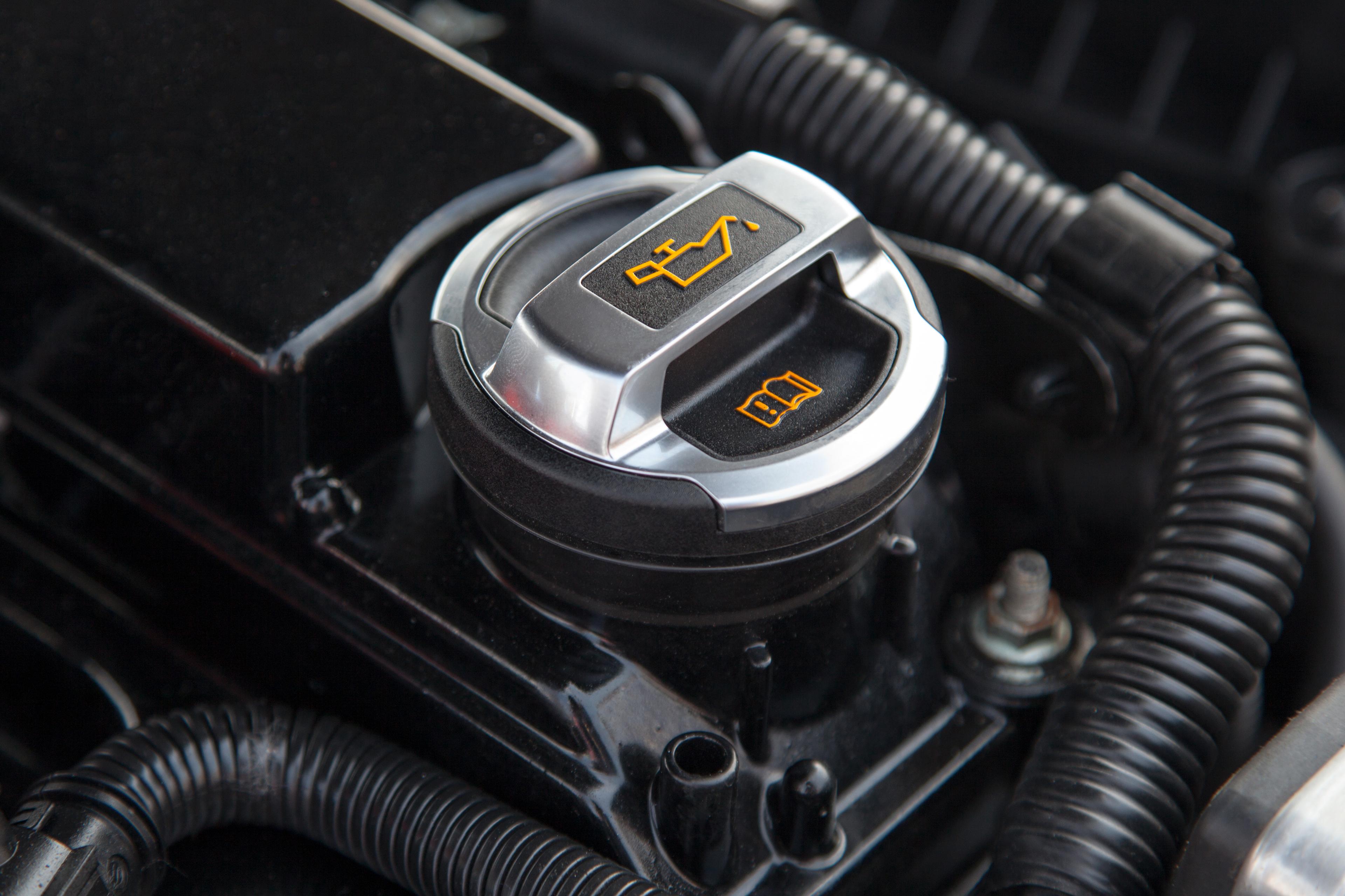 The opening for a car's oil tank, under the hood of the car. Surrounding the opening are various hoses and parts that make up the car's engine.