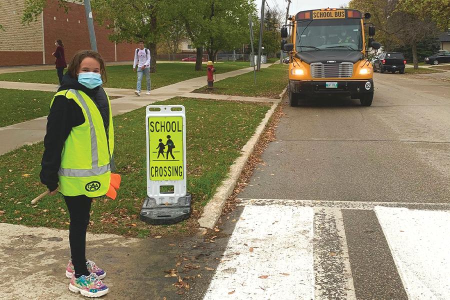 A girl wearing a face mask standing in front of a school bus.