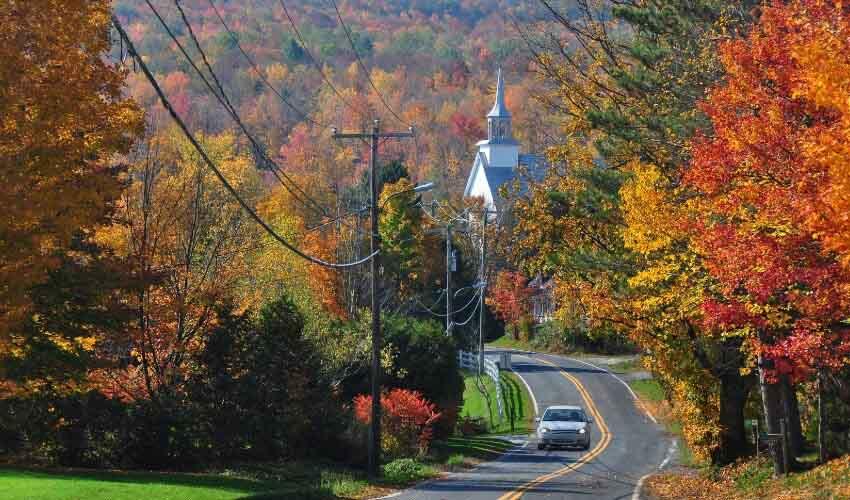 A road lined with fall colored trees and a church.