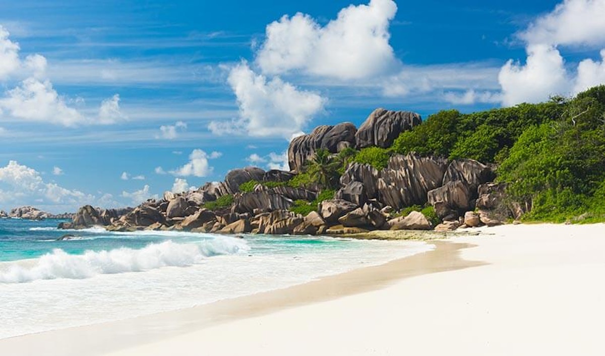 A beach with white sand and rocks in the background.