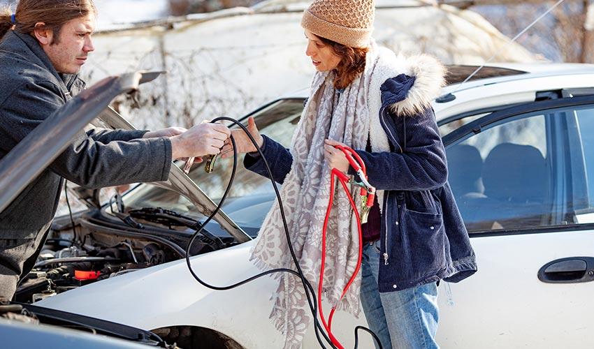 A man and a woman working on a car battery.