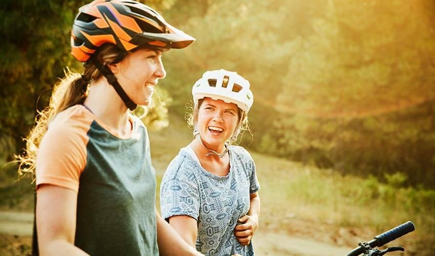 Two women riding bikes in the woods.