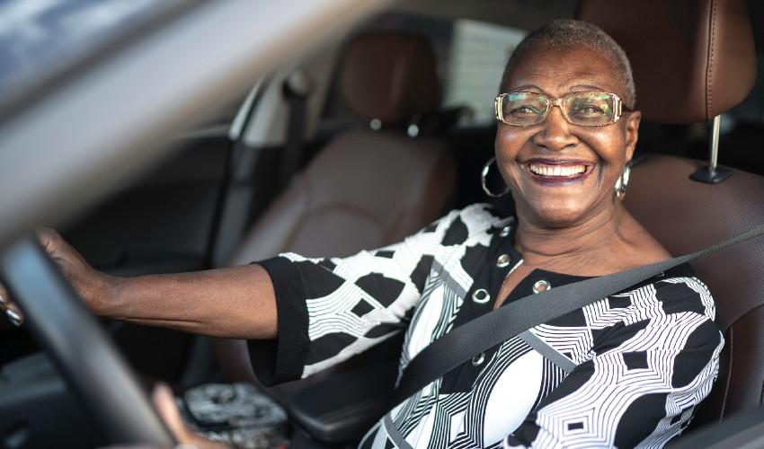 An older woman smiling in the driver's seat of a car.