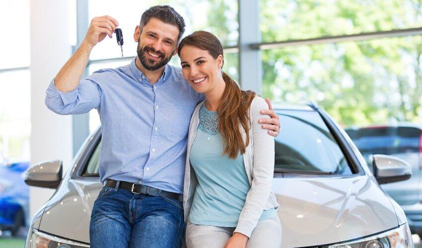 Happy couple holding car keys in car showroom stock photo.