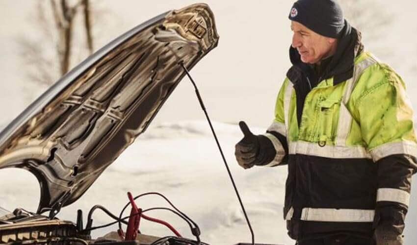 A man standing in the snow with his car's hood open.