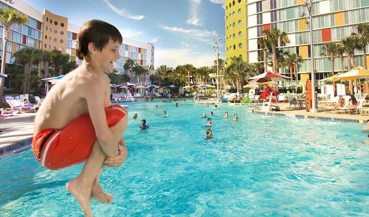 A boy jumping into a pool at a resort.