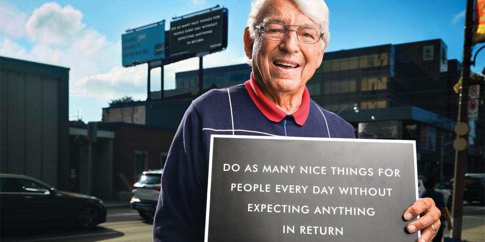 A man holding a sign that says do many nice things for people every day without expecting anything in berlin.
