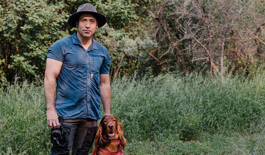 A man standing next to a dog in the woods.