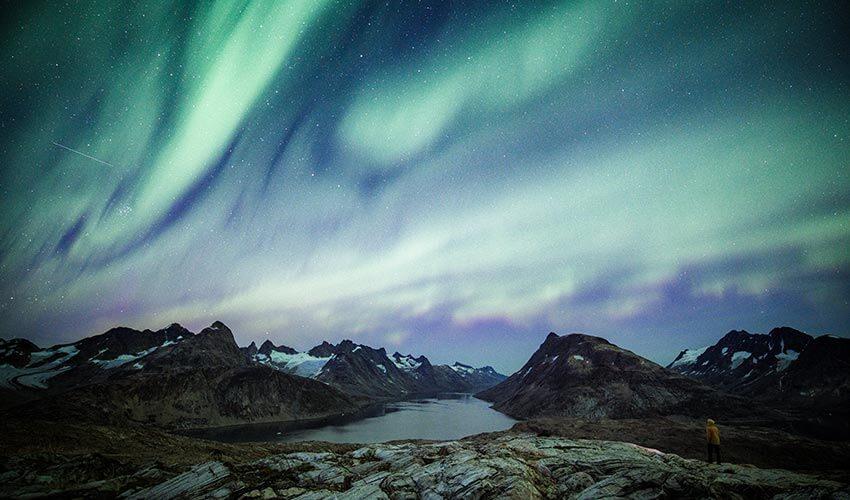 The aurora borealis over a lake and mountains.