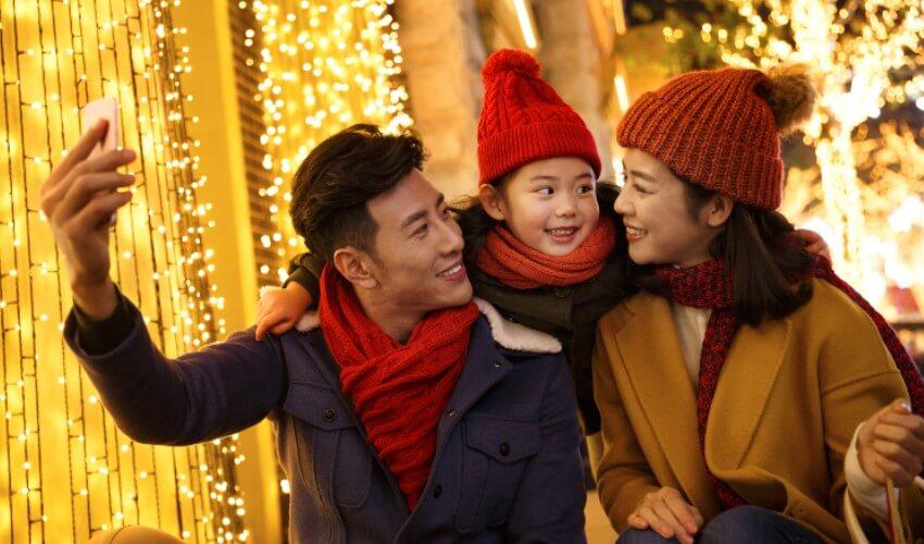 A family is taking a selfie in front of christmas lights.