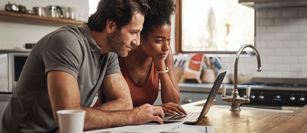 A couple sits at a table, looking at a laptop screen.