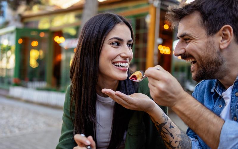 A man and a woman, the man is sharing a bite of food on a spoon with her.