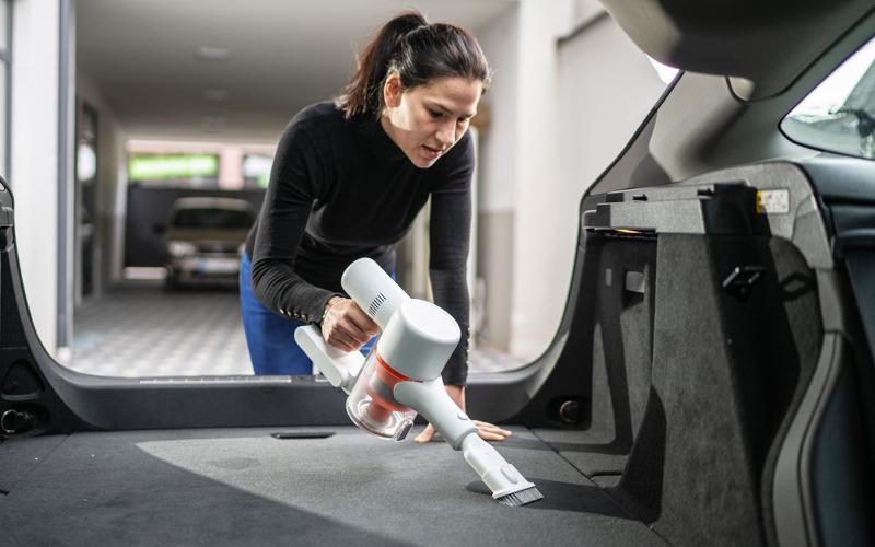 Woman with using a small handheld vacuum in the trunk of a car
