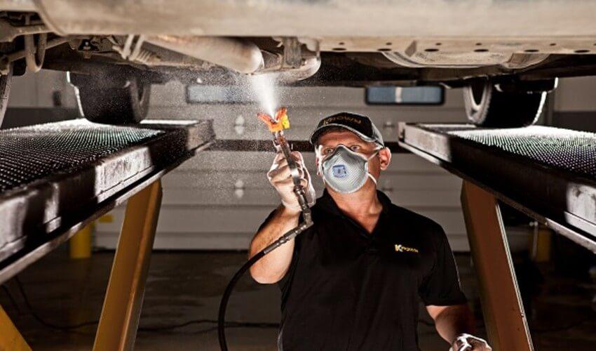 Auto technician applying undercoating to a vehicle's chassis.