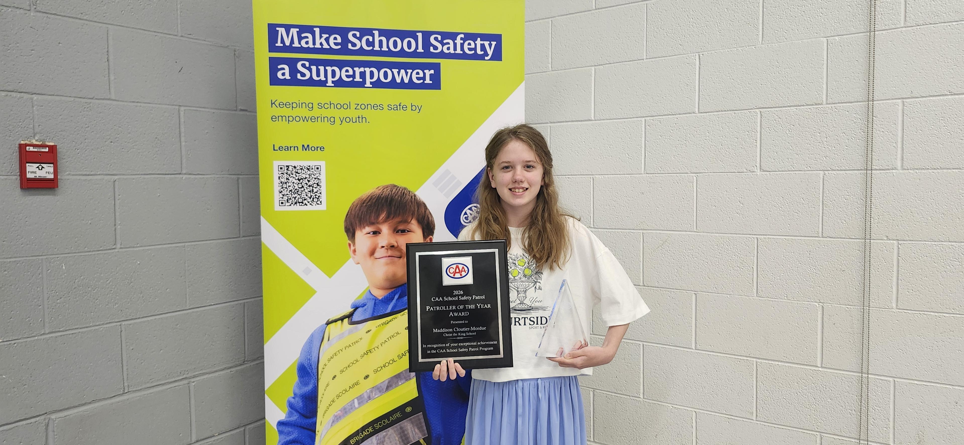 A young girl wearing a white graphic t-shirt and a blue skirt accepts an award plaque from CAA.