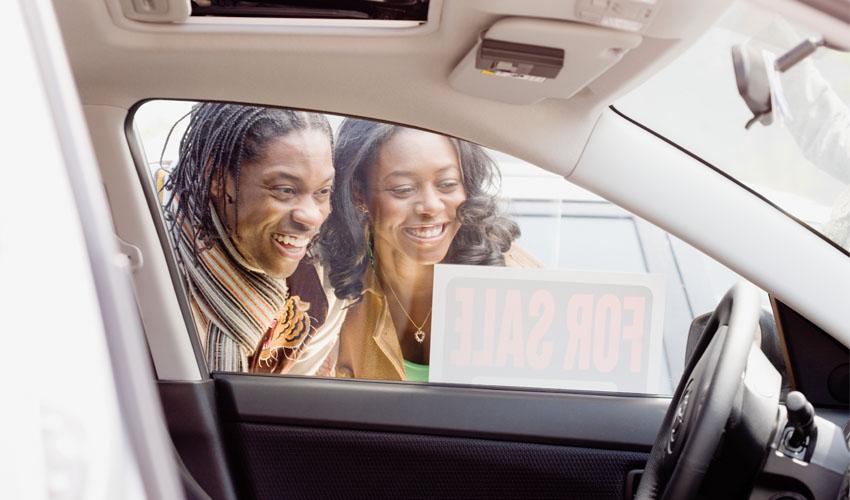 Two people in a car with a for sale sign.