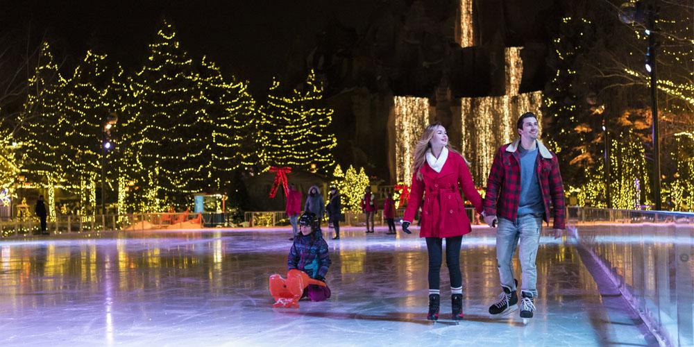 People ice skating at an outdoor rink with festive lights at night.