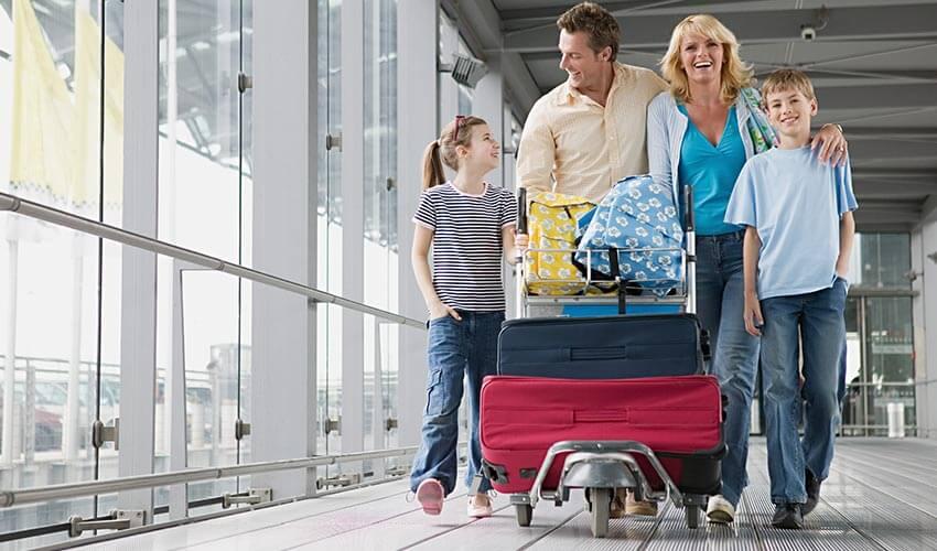 A family of four walking through an airport terminal with luggage.