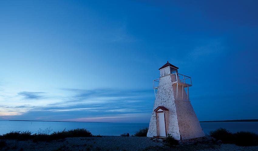 A solitary lighthouse stands against a dusky blue sky by a calm sea.