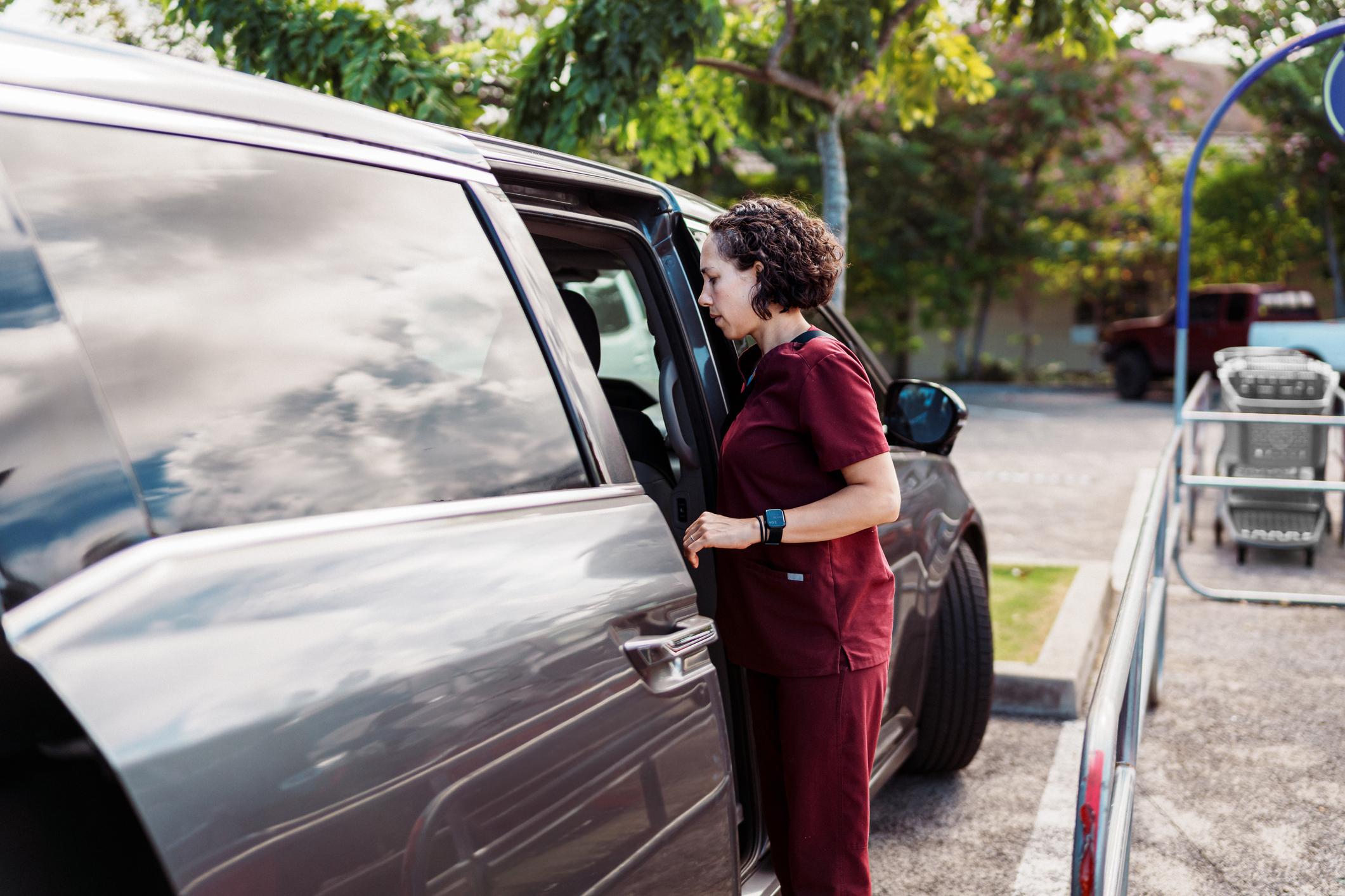 Woman looking inside her back seat from the open door in a shopping parking lot.