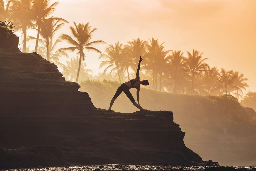 A woman is doing yoga on a cliff overlooking the ocean.