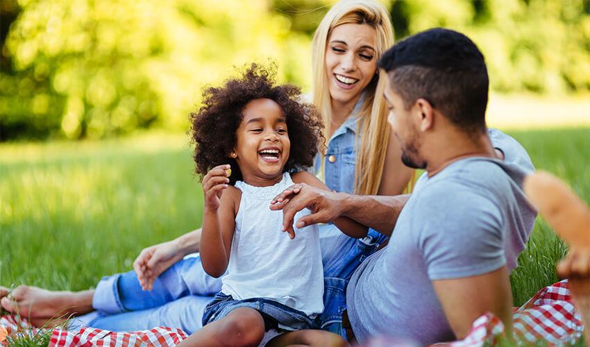A family sitting on a picnic blanket in a park.