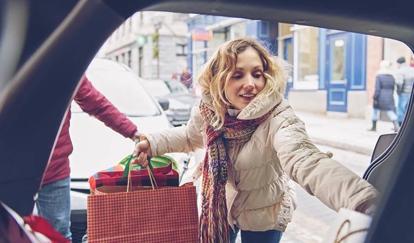 A woman is getting out of a car with shopping bags.