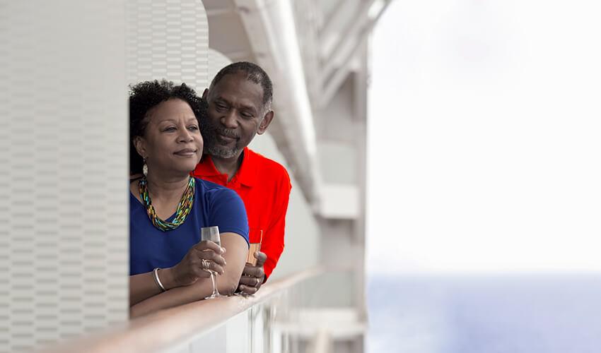A couple on a cruise ship leaning against a railing.