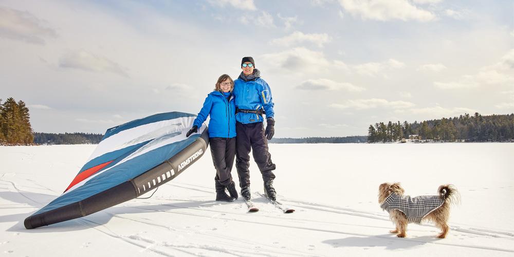 Two people with a kite and a dog on a snowy landscape.