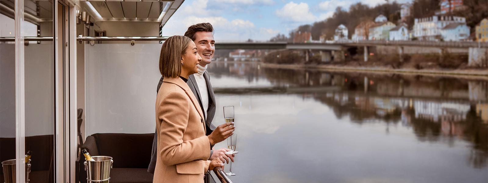 A stylish couple in coats drinking champagne on a river cruise ship deck
