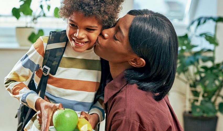 A woman kisses her son while holding an apple.